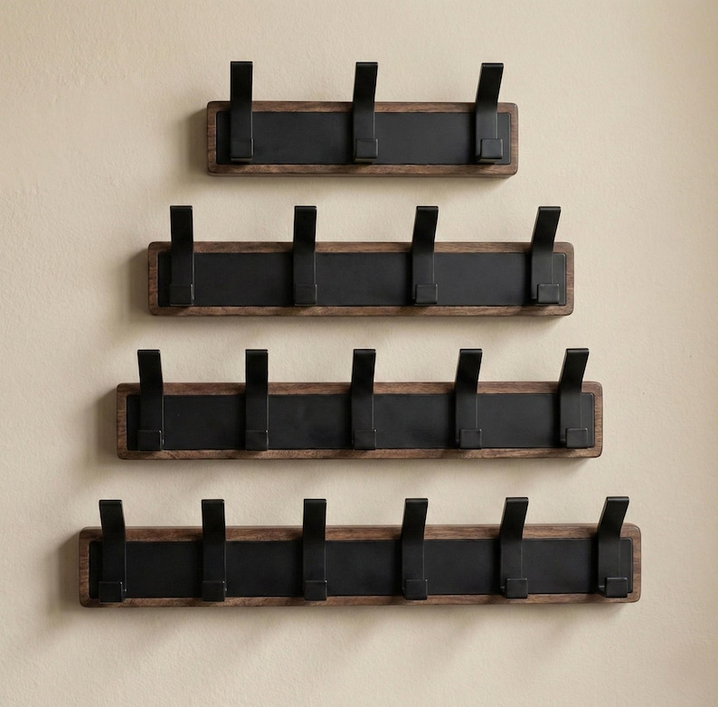 Pu&ograve; includere: Quattro attaccapanni in legno con ganci in metallo nero sono montati su una parete beige. Ogni attaccapanni ha una cornice in legno marrone scuro con un pannello centrale nero e ganci distanziati. Le dimensioni variano, con 3-6 ganci.