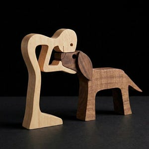 May include: A wooden sculpture of a person embracing a dog. The person is light-colored wood, while the dog is a darker wood. The sculpture is on a dark surface with a black background. The dog has large ears and a tail.