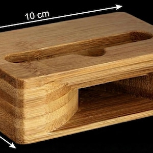 May include: A rectangular bamboo phone stand, 10 cm long, 6 cm wide, and 3 cm high. It features a slot for a phone and a rounded cutout. The natural wood grain is visible, and the stand is designed for desk or table use.