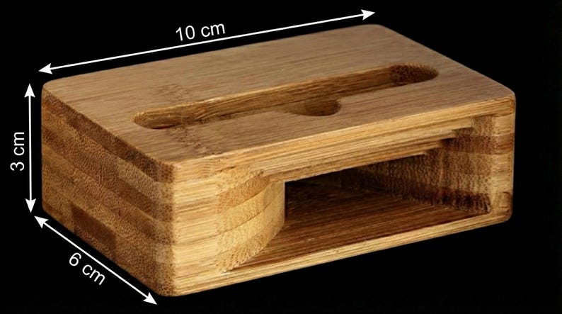 May include: A rectangular bamboo phone stand, 10 cm long, 6 cm wide, and 3 cm high. It features a slot for a phone and a rounded cutout. The natural wood grain is visible, and the stand is designed for desk or table use.
