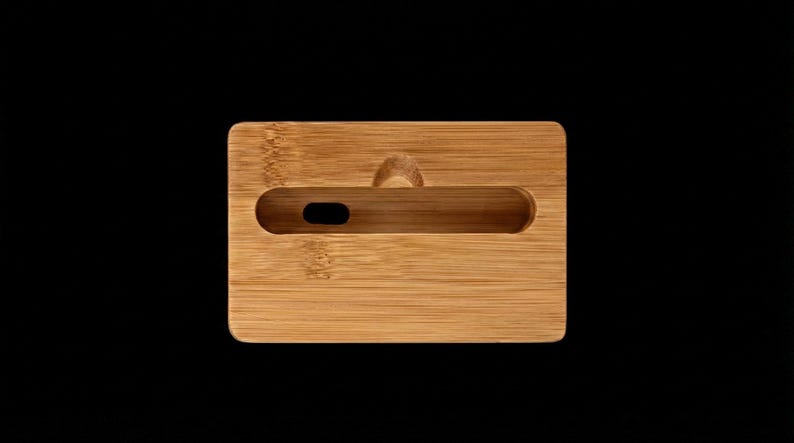 May include: A rectangular bamboo phone stand with a slot for a phone and a small hole for a charging cable. The stand has a natural wood grain finish and a small handle on the top. The stand is on a black background.
