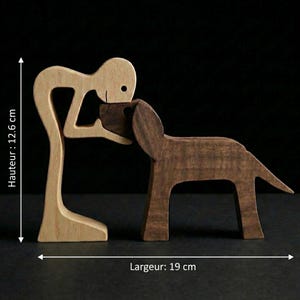 May include: A wooden sculpture depicting a person embracing a dog. The person is light-colored wood, while the dog is a darker brown. The sculpture is approximately 5 inches tall and 7.5 inches wide, showcasing a loving bond.