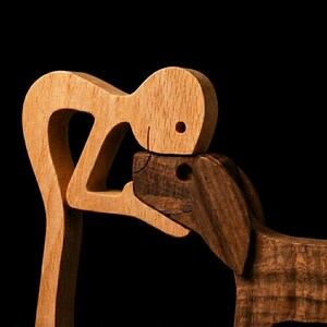 May include: Wooden sculpture depicting a person embracing a dog. The person is crafted from light-colored wood, while the dog is made of darker wood. The sculpture is set against a black background, highlighting the contrast in colors and textures.