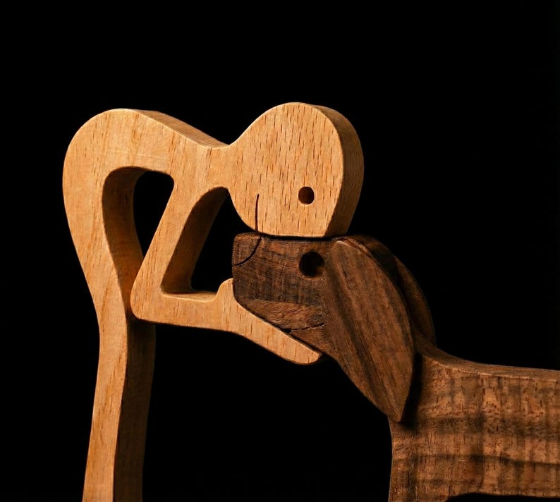 May include: Wooden sculpture depicting a person embracing a dog. The person is crafted from light-colored wood, while the dog is made of darker wood. The sculpture is set against a black background, highlighting the contrast in colors and textures.