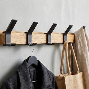 Peut inclure: Un porte-manteau mural en bois avec quatre crochets en métal noir. Un manteau gris foncé est suspendu à un crochet, et un sac fourre-tout beige et une écharpe beige sont suspendus aux autres crochets.