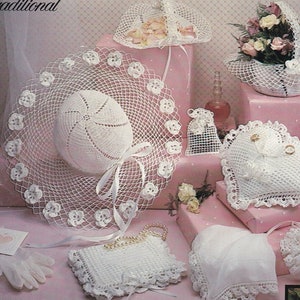 May include: A collection of crocheted wedding accessories in white, including a hat, a basket, a pillow, and a ring bearer pillow. The items are arranged on a pink and wooden surface. The text "Traditional" and "Victorian" are visible in the image.