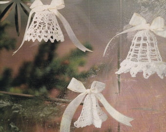 May include: Three white crocheted bells with white satin ribbon bows. The bells are hanging from a window.
