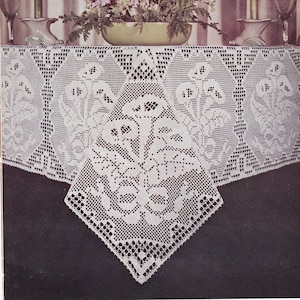 May include: A white crocheted tablecloth with a floral design. The tablecloth is laid on a table with a bouquet of pink flowers in a green bowl and two candlesticks with green candles.