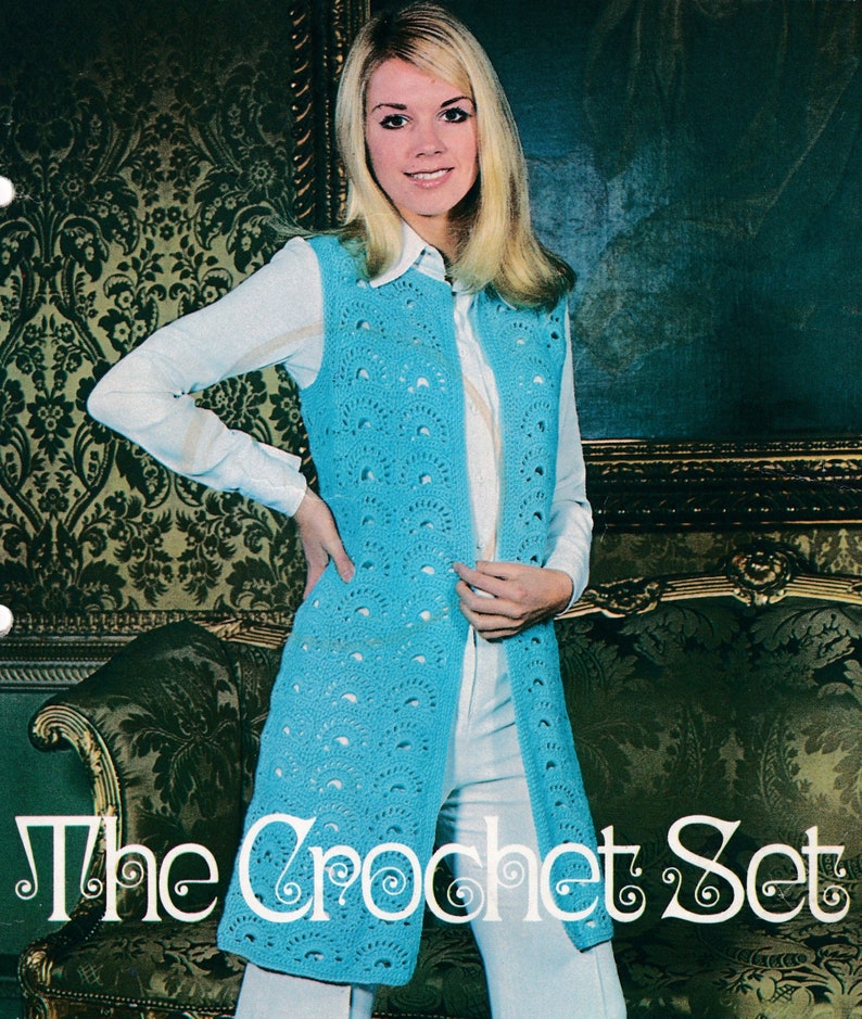 Op de afbeelding: Een vrouw draagt een lange, lichtblauwe gehaakte vest met een wit shirt en een witte broek. De vest heeft een gegolfd ontwerp en is open aan de voorkant. De tekst "The Crochet Set" is zichtbaar onderaan de afbeelding.