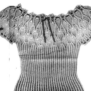 Pode incluir: Um top branco de crochê com decote festoneado e mangas curtas. O top tem um delicado padrão de renda e um laço no decote.