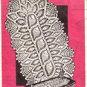 May include: A white crocheted lace doily with a scalloped edge, hanging on a wall above a dark wooden table with a smaller crocheted lace doily on top. Two candlesticks are on the table.