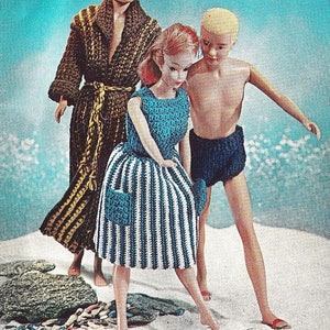 May include: Three dolls dressed in crocheted clothing stand on a white sandy beach. The doll on the left is wearing a brown and gold crocheted robe. The doll in the center is wearing a blue and white striped crocheted dress. The doll on the right is wearing blue crocheted swim trunks.