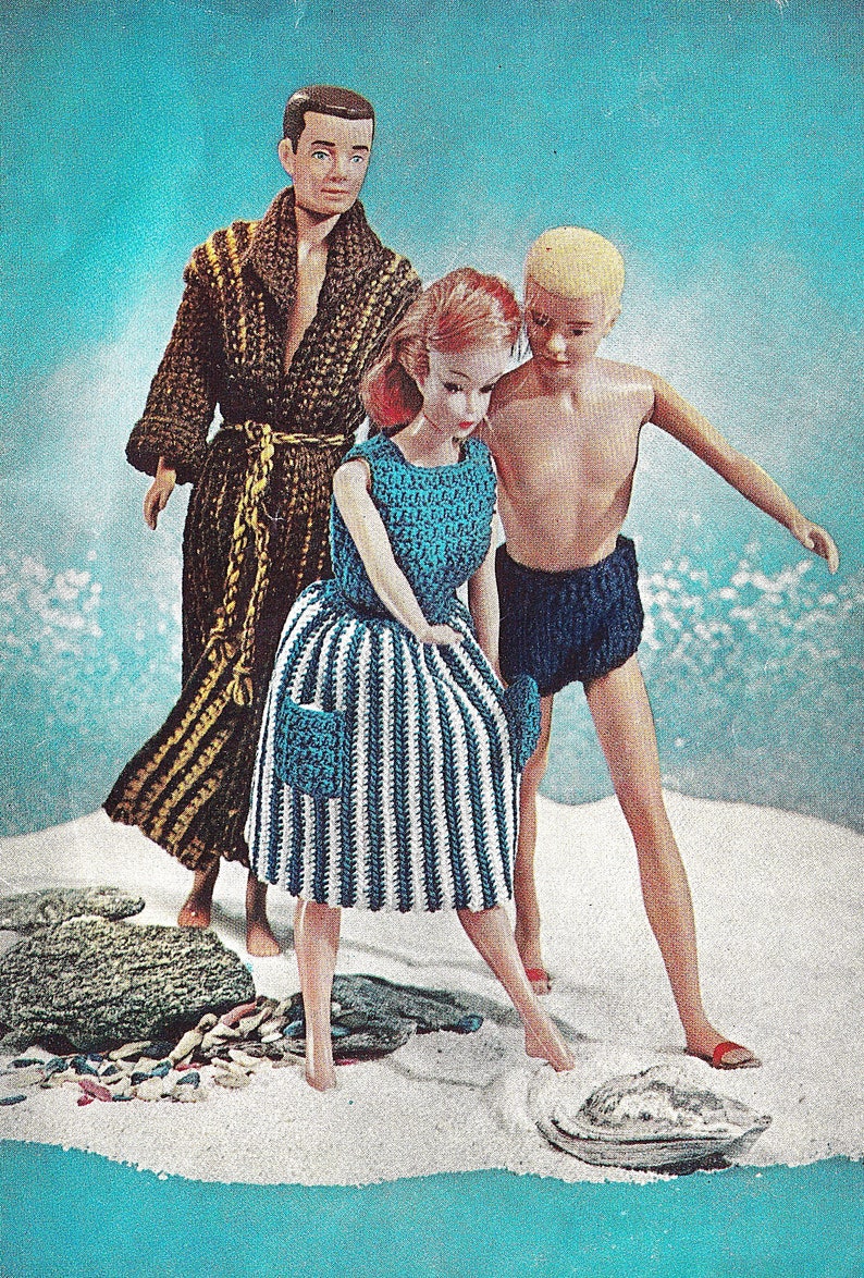 May include: Three dolls dressed in crocheted clothing stand on a white sandy beach. The doll on the left is wearing a brown and gold crocheted robe. The doll in the center is wearing a blue and white striped crocheted dress. The doll on the right is wearing blue crocheted swim trunks.