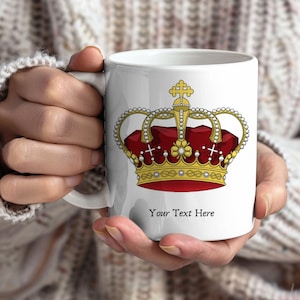 Könnte beinhalten: Weiße Keramiktasse mit einem goldenen und roten Design einer königlichen Krone. Die Krone hat ein rotes Samtinterieur, goldene Details und ist mit Perlen und Kreuzen verziert. Der Text "Your Text Here" ist darunter gedruckt.
