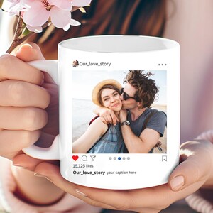 May include: White ceramic mug featuring a photo of a couple embracing and kissing. The mug has an Instagram-style design with the text "Our_love_story" and "15,125 likes". The mug is held by a person.