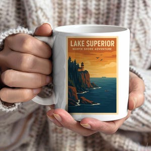 Peut inclure: Mug en céramique blanche avec une illustration de la côte nord du lac Supérieur. Le design comprend un phare sur une falaise, des arbres et le texte "Lake Superior North Shore Adventure" dans un style vintage.