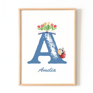 Könnte beinhalten: Gerahmter Druck mit dem blauen Buchstaben "A", verziert mit einem Tulpenstrauß und einem Marienkäfer. Der Name "Amelia" steht darunter. Geeignet für ein Kinderzimmer, in einem Holzrahmen.