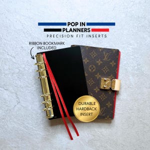 Könnte beinhalten: Ein schwarzer Planer mit goldenem Binder und rotem Schleifenlesezeichen. Der Planer hat einen braunen, gemusterten Einband mit goldenem Verschluss. Der Text auf dem Bild lautet "POP IN PLANNERS" und "PRECISION FIT INSERTS". Ein goldener Aufkleber sagt "DURABLE HARDBACK INSERT".
