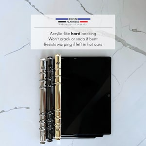 May include: Three rectangular black planner inserts with metallic ring binders in silver, black, and gold. The text reads: POP IN PLANNERS PRECISION FIT INSERTS. Acrylic-like hard backing. Won't crack or snap if bent. Resists warping if left in hot cars.