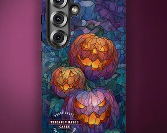 May include: A rectangular phone case featuring a stained-glass style design of three glowing jack-o'-lanterns in shades of orange and purple, surrounded by dark blue and teal foliage. The text "TEXCAJUN BAYOU CASES" is printed in a circular logo.