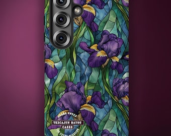 Puede incluir: Una funda para teléfono con un patrón de vidrieras de lirios morados con centros amarillos y tallos verdes. El diseño incluye un logotipo circular con el texto TEXCAJUN BAYOU CASES FOR EVERY OCCASION. Tiene un recorte para triple cámara.