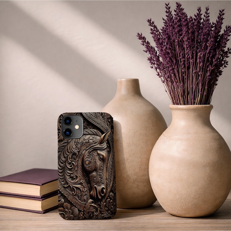 Peut inclure: Une coque de t&eacute;l&eacute;phone rectangulaire pr&eacute;sentant un relief d&eacute;taill&eacute; de t&ecirc;te de cheval entour&eacute; de motifs floraux et de volutes complexes dans des tons brun fonc&eacute; et bronze, avec une d&eacute;coupe pour double objectif photo en haut &agrave; gauche.