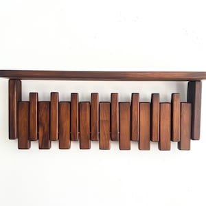 May include: A dark brown wooden wall shelf with a horizontal top and a series of vertical wooden slats below. The shelf is mounted on a white wall, showcasing a minimalist design.