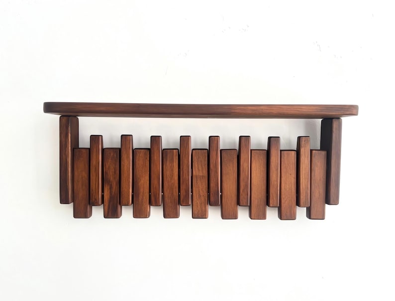 May include: A dark brown wooden wall shelf with a horizontal top and a series of vertical wooden slats below. The shelf is mounted on a white wall, showcasing a minimalist design.