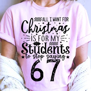 Peut inclure: Un t-shirt rose clair avec le texte "ALL I WANT FOR Christmas IS FOR MY Students to stop saying 67" en noir. Le t-shirt a des manches retroussées.