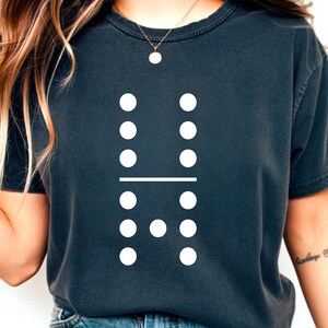 Peut inclure: T-shirt gris foncé avec un motif de domino blanc. Le motif de domino comporte six points blancs de chaque côté, séparés par une ligne blanche. Le t-shirt est de style décontracté et confortable.