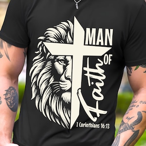 Peut inclure: T-shirt noir avec une tête de lion et une croix. Le texte indique "MAN OF Faith" avec le verset biblique "1 Corinthiens 16:13" en dessous. Le graphisme est blanc.