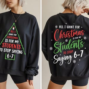 Peut inclure: Sweat-shirt noir avec un motif de sapin de Noël sur le devant, avec le texte "All I want for Christmas is for my students to stop saying 6-7." Le dos du sweat-shirt porte le même message. Un vêtement de fête.