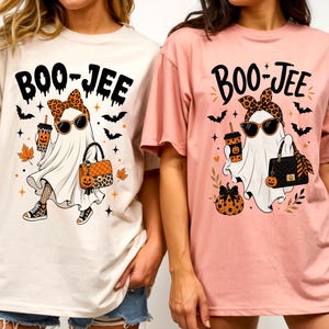 Peut inclure: Deux t-shirts à manches courtes, un crème et un rose clair, arborant chacun le dessin d'un fantôme portant des lunettes de soleil, un bandeau léopard, tenant un gobelet et un sac à main. Le texte BOO-JEE est imprimé au-dessus avec des chauves-souris.