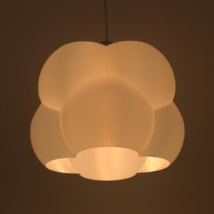 May include: A white, spherical pendant light fixture with a textured surface. The light has a unique, multi-lobed design, with a warm glow emanating from within. The fixture is suspended from a single cord, creating a modern aesthetic.