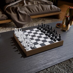 May include: A modern chess set with a brown wooden frame. The chessboard features a black and white checkered pattern. The chess pieces are stylized, with white and black figures arranged on the board. The set is displayed on a dark gray table.