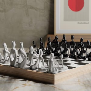 May include: A modern chess set with black and white pieces on a checkered board. The chess pieces are stylized human figures. The board is set on a wooden base. A framed artwork is in the background.