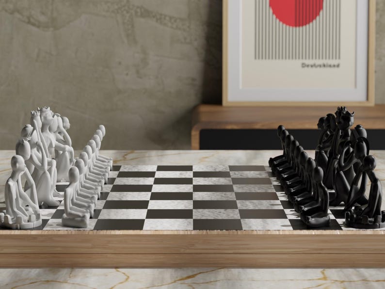 May include: A chess set with white and black pieces arranged on a checkered board. The pieces are stylized human figures. The board is set on a wooden frame. A framed print with a red circle and the word "Deutschland" is in the background.