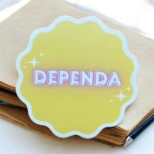 May include: A yellow sticker with a scalloped edge and the word "DEPENDA" in white and purple lettering. The sticker has a light blue border and star accents. The sticker is on a brown notebook.