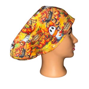 May include: A scrub cap featuring a vibrant yellow and orange autumn-themed print. The pattern displays pumpkins, fall foliage, and white ghost figures holding coffee cups. The text "PUMPKIN PATCH" is printed in black on wooden-style signs.