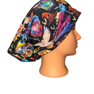 May include: Black scrub cap featuring colorful illustrations of owls, crests, and other magical elements. The cap has a gathered design and is made of a soft, flexible fabric. The cap is designed to be worn during medical procedures.