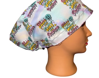 May include: A white scrub cap with a colorful, tie-dye-like background. The cap is patterned with the phrase "Have the Day You Deserve" in yellow, pink, and teal, along with smiley face graphics.