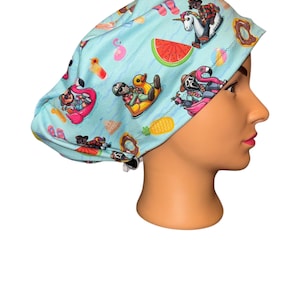 May include: A light blue surgical scrub cap with a fun summer-themed pattern. The pattern includes images of a watermelon slice, donuts, a flamingo, and a unicorn riding an inflatable float. The cap is designed to cover the hair.