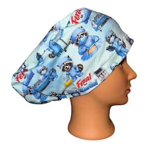 May include: A light blue scrub cap featuring a repeating pattern of cartoon raccoons dressed in medical scrubs, masks, and surgical caps. The fabric includes the text Feral but Sterile! in red and blue script, along with medical equipment icons.