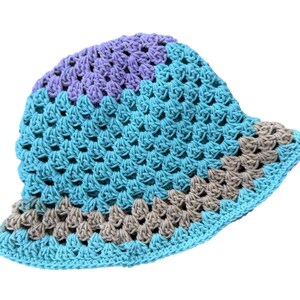 May include: A crocheted bucket hat in shades of blue, purple, and gray. The hat features a textured, open weave design. The brim is a solid color, while the crown is divided into sections of different colors.