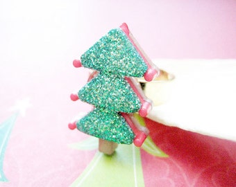 May include: A sparkly green Christmas tree ring with pink accents. The ring is made of plastic and is a fun and festive accessory.