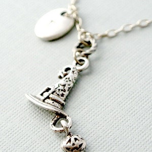 Puede incluir: Un collar de plata con un dije de sombrero de bruja y un dije de calabaza. El collar también tiene un dije ovalado de plata con la letra "A" en él.