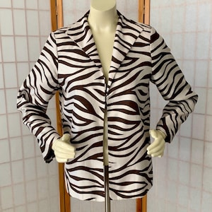 May include: A zebra-print blazer in brown and white, displayed on a mannequin. The jacket features a classic lapel and long sleeves. The bold pattern creates a striking visual statement, suitable for a variety of outfits.