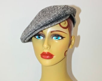 May include: A gray tweed newsboy cap. The cap is angled on a mannequin head with blue eyes and red lips. The hat has a classic, rounded shape and a small brim. The fabric has a textured appearance.
