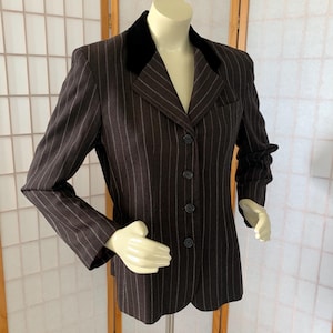 May include: A brown pinstripe blazer with a black velvet collar. The blazer has a three-button closure and a single pocket. The pinstripes are a light gray color.