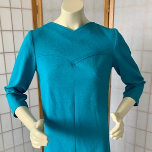 May include: A teal blue, long-sleeved dress with a V-neckline and a textured fabric.